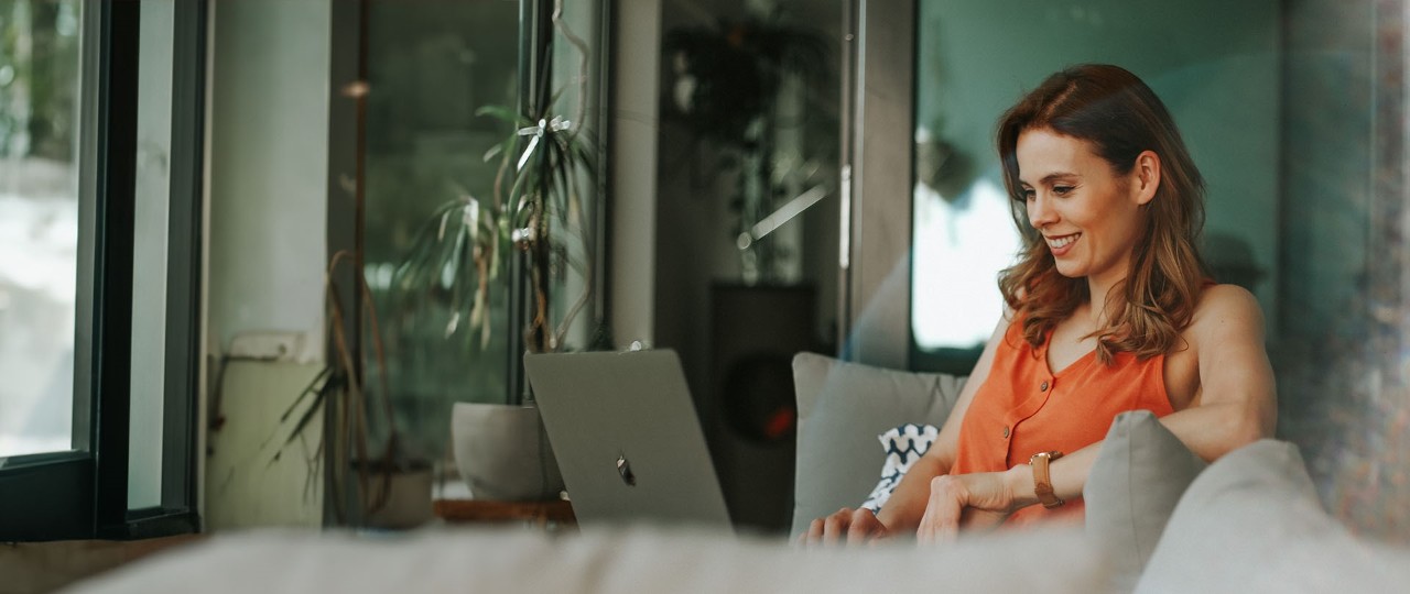 A woman on laptop smiling sat on a couch